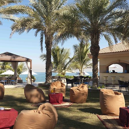 Al Raha Beach Resort & Spa Abu Dhabi Ristorante foto The photo depicts a beautiful outdoor setting with several elements of relaxation and leisure. In the foreground, there are large, comfortable bean bag chairs arranged on a grassy area, accompanied by low tables. Surrounding this seating area are tal