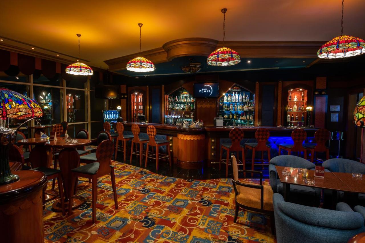 Al Raha Beach Resort & Spa Abu Dhabi Esterno foto The photo shows a cozy bar interior, featuring a well-stocked bar area with various bottles displayed on shelves. The bar is illuminated by colorful stained glass light fixtures, creating a warm and inviting atmosphere. The floor is covered with a vi