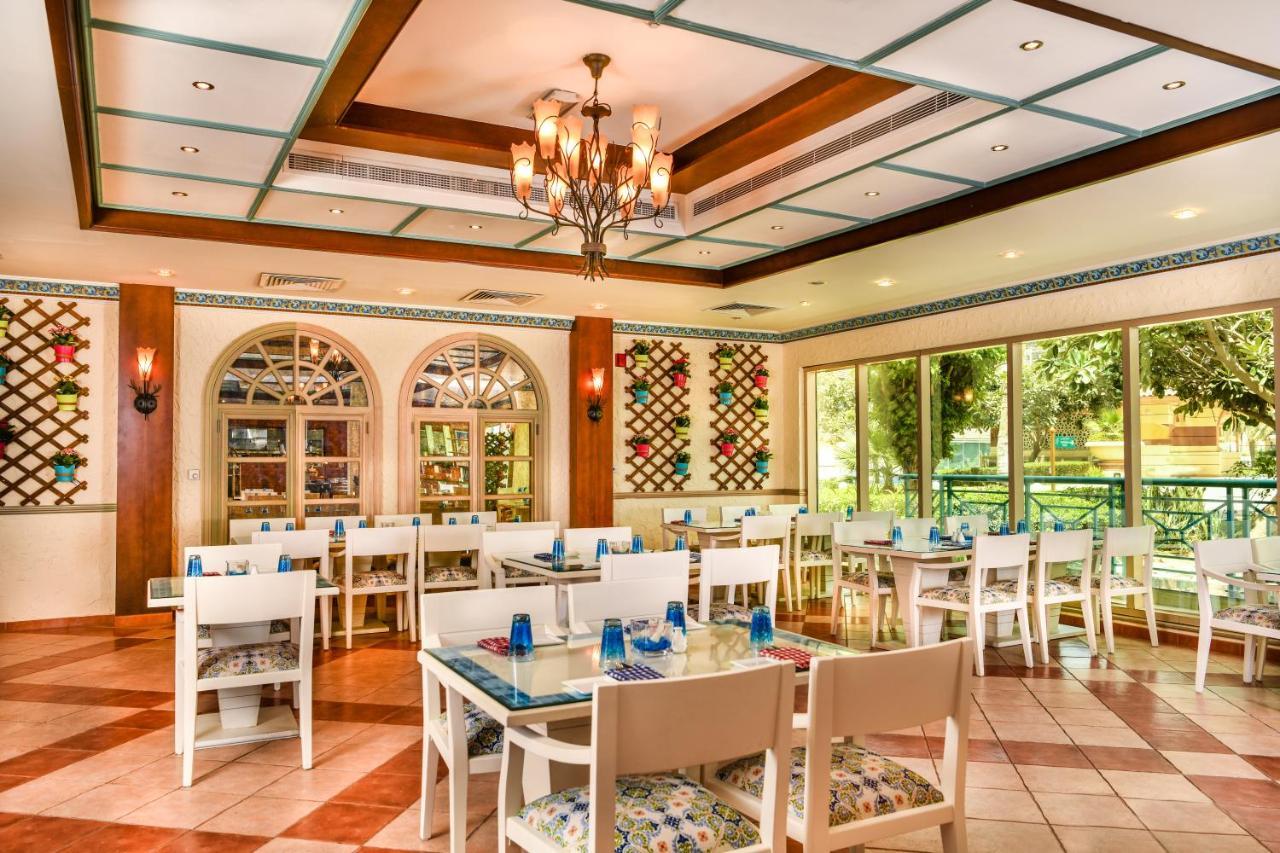 Al Raha Beach Resort & Spa Abu Dhabi Esterno foto The photo shows the interior of a restaurant or dining area. The space has a warm and inviting atmosphere, featuring a mix of decorative elements. 

- **Seating**: There are several white wooden tables and chairs arranged throughout the area, some wi