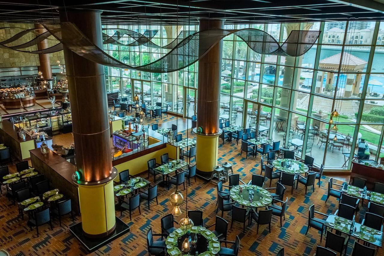 Al Raha Beach Resort & Spa Abu Dhabi Esterno foto The photo shows the interior of a restaurant with a modern design. It features large windows allowing natural light to flood the space, creating an inviting atmosphere. The dining area is furnished with round tables covered with green tablecloths and