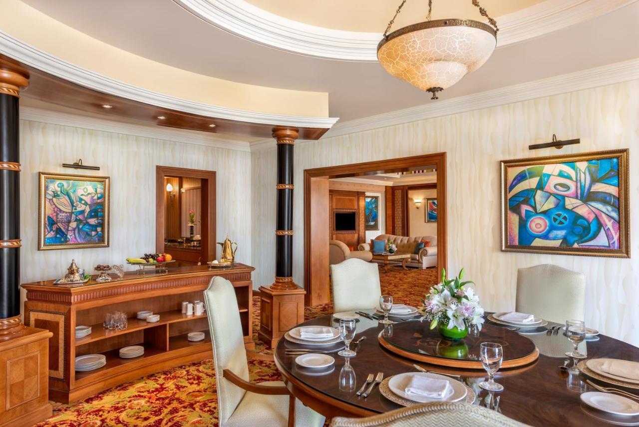Al Raha Beach Resort & Spa Abu Dhabi Esterno foto The photo shows an elegantly designed dining area and a glimpse into a luxurious living space. 

In the foreground, a round dining table is set with fine china, glassware, and a centerpiece featuring fresh flowers. The chairs surrounding the table ha