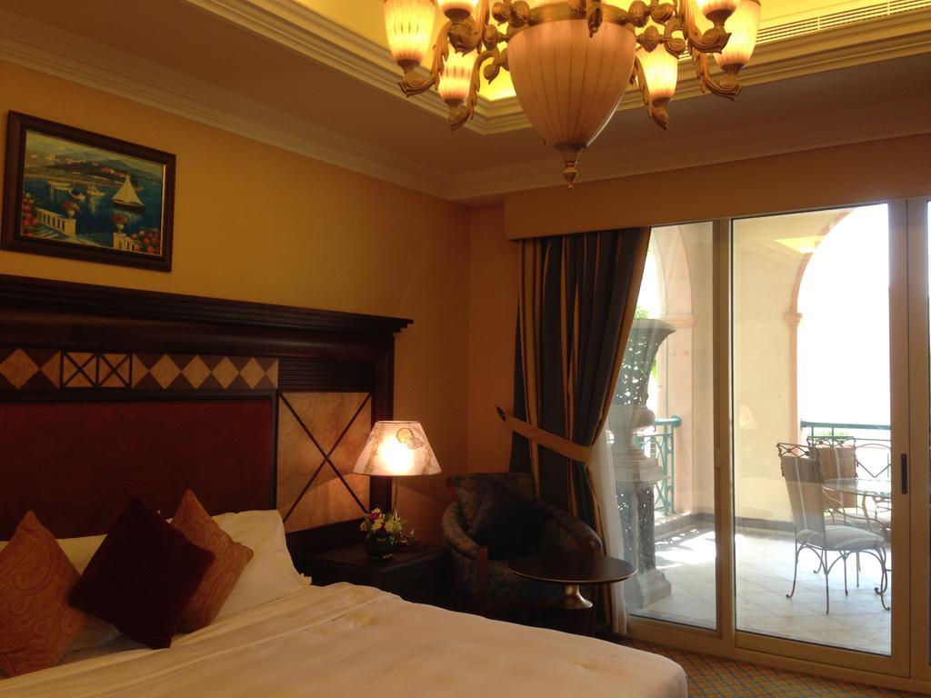 Al Raha Beach Resort & Spa Abu Dhabi Esterno foto The photo shows the interior of a hotel room. The room features a large bed with decorative cushions and a wooden headboard. There's a bedside lamp emitting a warm light, and a painting is hung on the wall above the bed. To the right, there's a windo