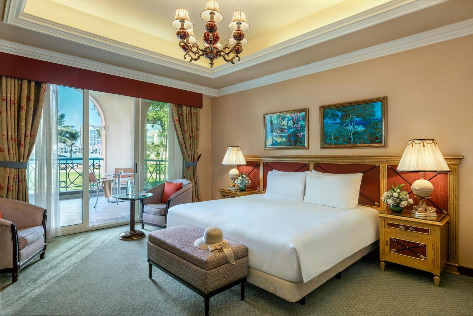 Al Raha Beach Resort & Spa Abu Dhabi Esterno foto The image depicts a well-furnished hotel room. It features a large bed with white linens, flanked by two bedside lamps. Above the bed, there are two pieces of artwork hanging on the walls. To the side, there is a comfortable armchair and a small tabl