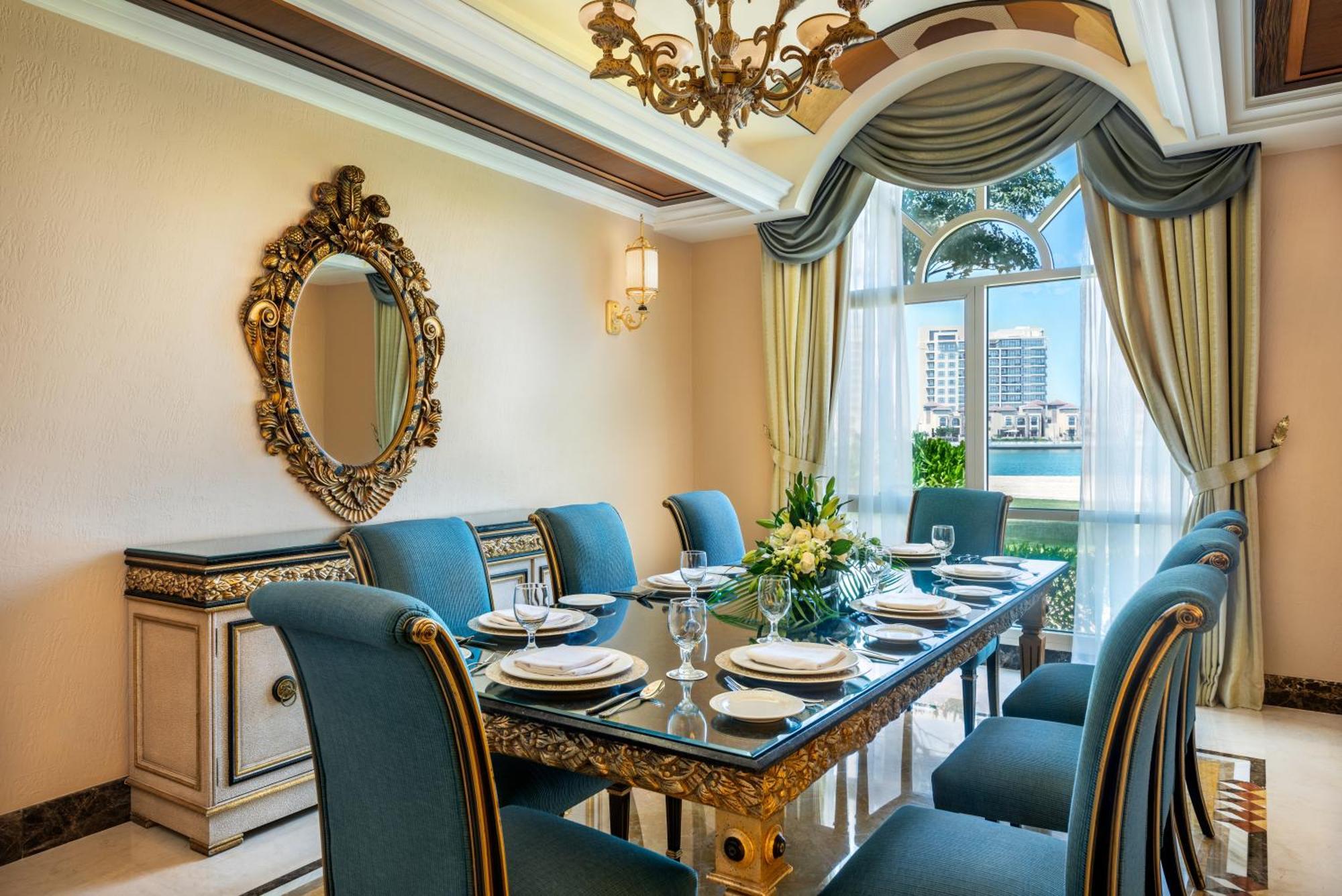 Al Raha Beach Resort & Spa Abu Dhabi Esterno foto The photo features an elegantly decorated dining room. It includes a long, polished table set for a meal with plates, glasses, and decorative items, surrounded by plush blue chairs. The room is adorned with sophisticated details, such as an ornate mi