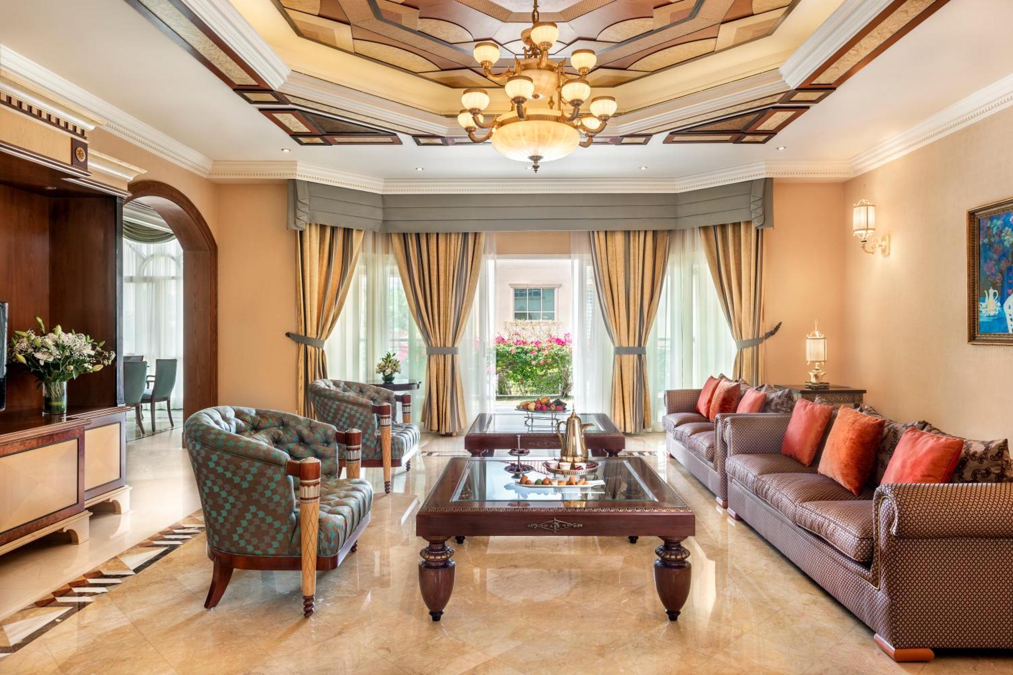 Al Raha Beach Resort & Spa Abu Dhabi Esterno foto The photo shows an elegantly designed living room. It features a high, intricately patterned ceiling with a chandelier hanging in the center. The room is filled with natural light from large windows covered with flowing curtains. 

There are two diff