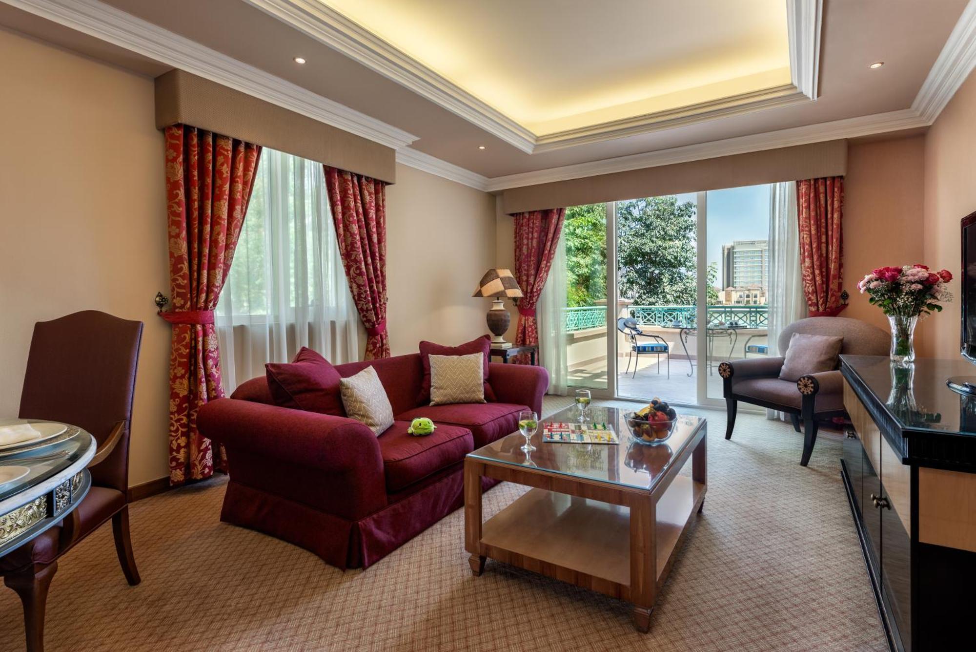 Al Raha Beach Resort & Spa Abu Dhabi Esterno foto The photo shows a well-decorated hotel room or living area. It features a cozy seating arrangement with a deep red couch adorned with cushions, paired with a single chair. There is a glass coffee table in front of the couch, which is set on a plush c