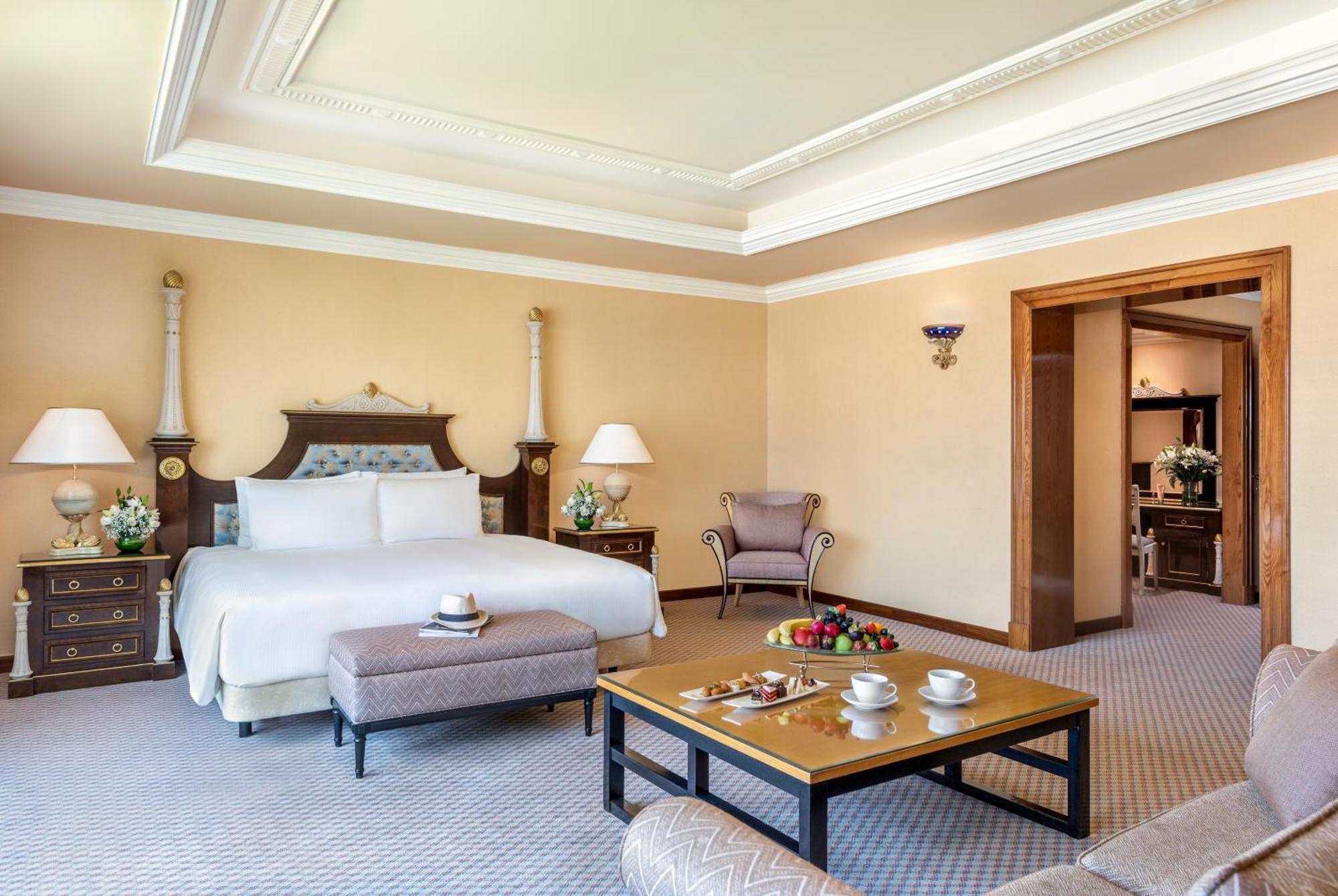 Al Raha Beach Resort & Spa Abu Dhabi Esterno foto The photo shows an elegant hotel room, featuring a large bed with white linens, flanked by stylish bedside tables and lamps. The room has a warm color palette, with light brown walls and a plush carpet. A comfortable armchair is positioned nearby, an