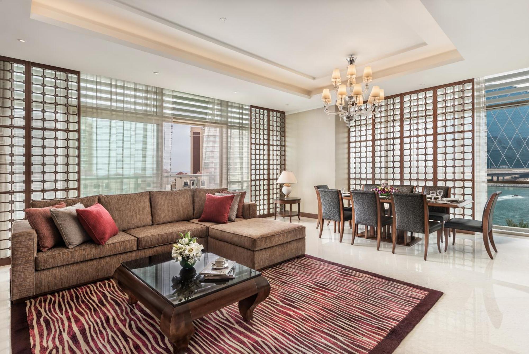 Al Raha Beach Resort & Spa Abu Dhabi Esterno foto The photo shows a stylish and modern living space. On one side, there is a comfortable sectional sofa in a brown upholstery, accented with red and gray cushions. In front of the sofa, there is a glossy black coffee table adorned with a small floral a