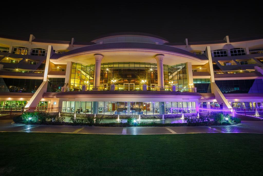 Al Raha Beach Resort & Spa Abu Dhabi Esterno foto The photo shows a modern architectural building illuminated at night. The structure has a large central entrance with multiple glass windows, flanked by symmetrical columns. The exterior features a combination of sleek lines and curves, with lighting